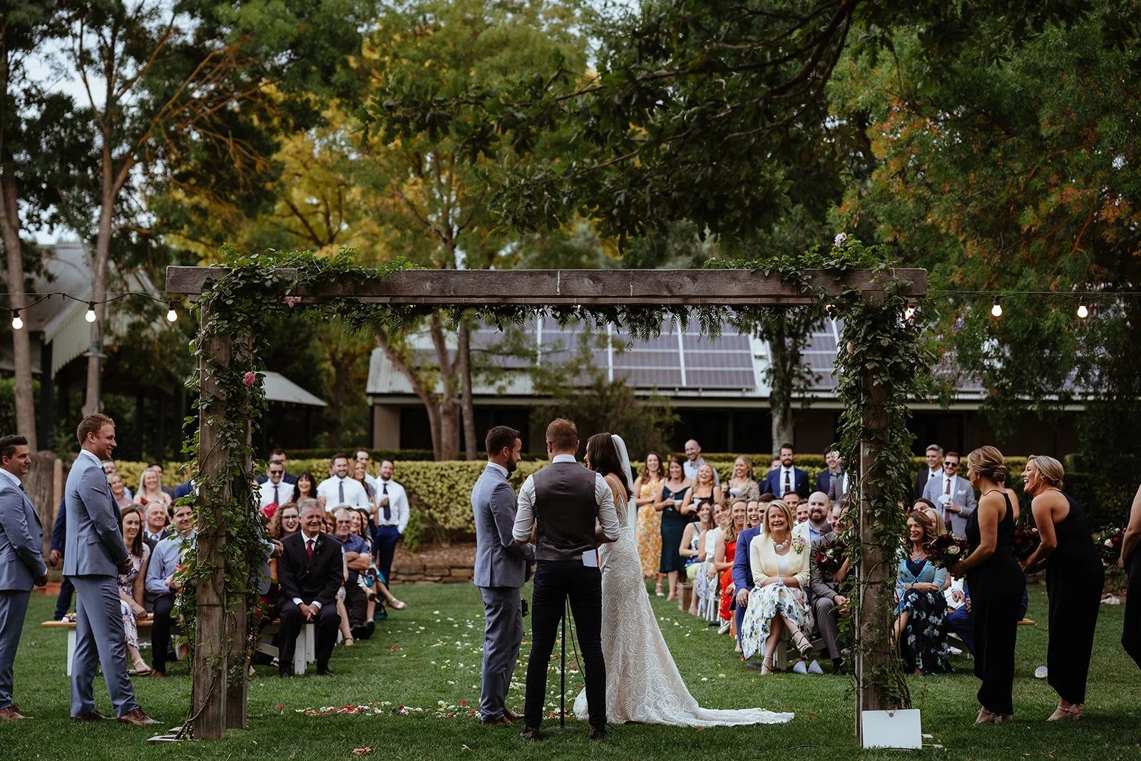 An outdoor wedding ceremony under a floral arbor